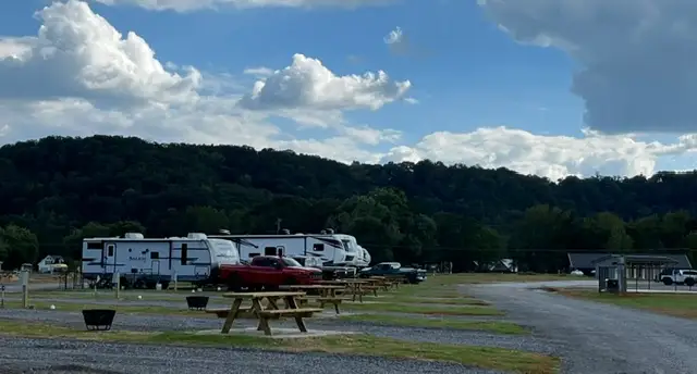 Gravel RV park with parked travel trailers, a red pickup truck, wooden picnic tables and black fire rings below