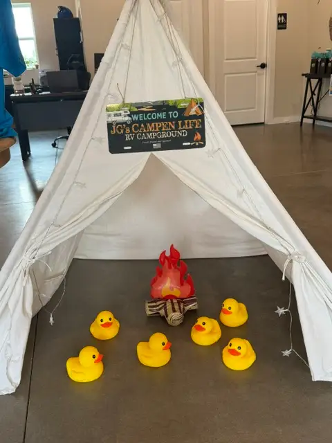 Indoor decorative canvas teepee display with a faux campfire, rubber ducks, and a "JG's Campen Life RV Campground"